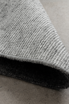 Close-up of a textured gray rug on a concrete floor laine 100% naturelle tapis fais a la main naturug hand made rug morocco maroc marocain naturug collection tapis berbère laine naturelle handmade Moroccan wool rug tapis marocain fait main berber rugs